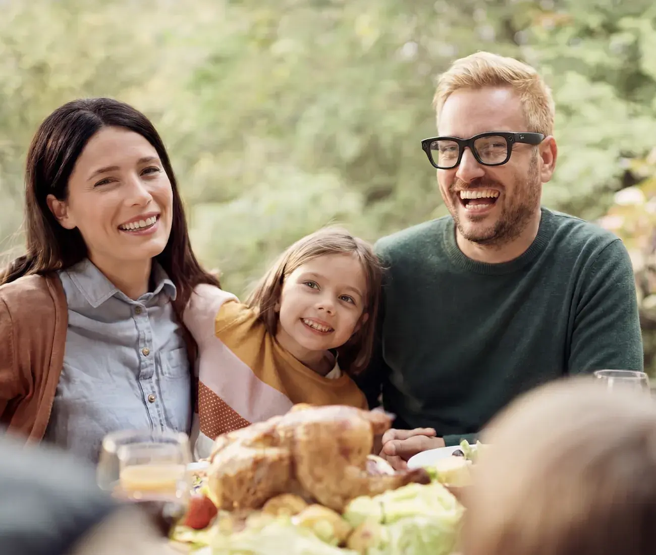 A father laughing at an outdoor family dinner while wearing black Meta smart glasses.