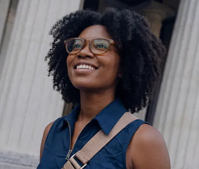 A smiling woman looking up while wearing translucent brown Meta smart glasses.