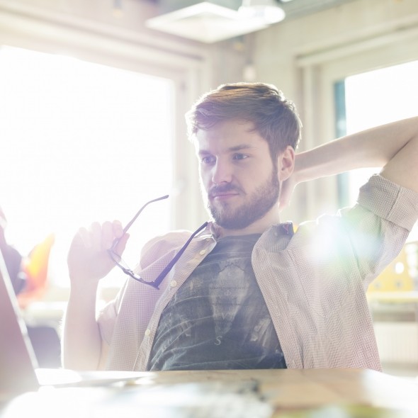 man looking at computer holding his glasses
