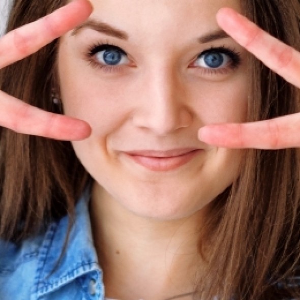 a women with brown hair in blue shirt holding up peace signs to her eyes 