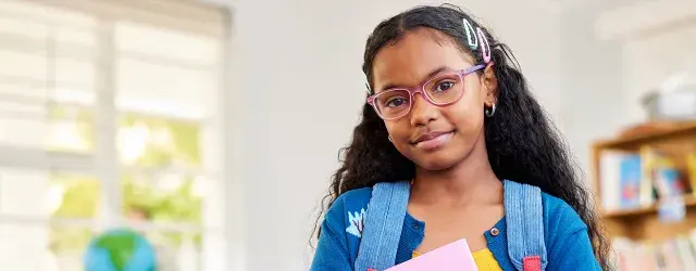 Young girl with glasses wearing backpack in classroom