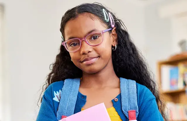 Young girl with glasses wearing backpack in classroom
