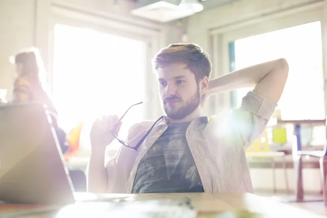 man looking at computer holding his glasses