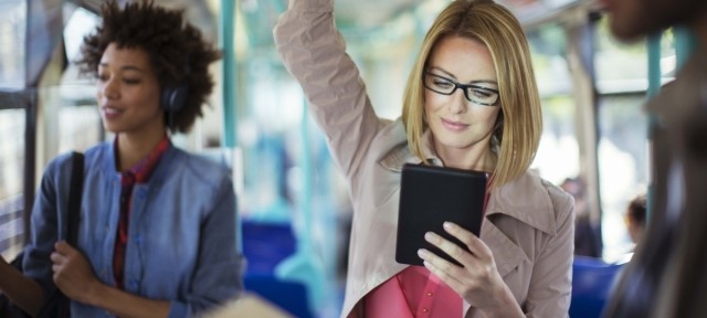 Woman wearing glasses on train reading tablet