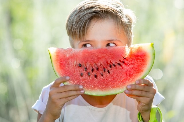 young boy hold a slice of watermelon in front of face