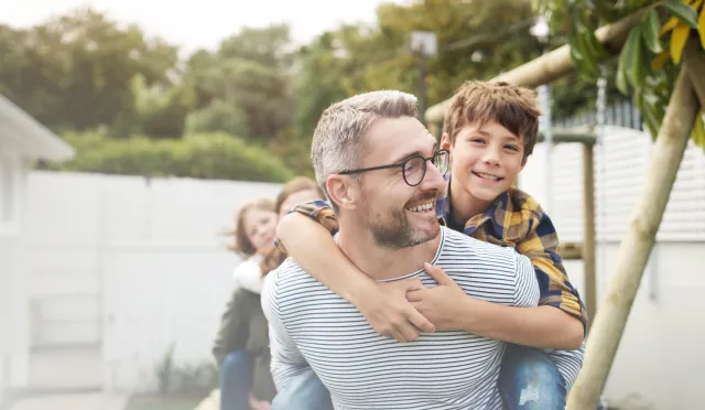 A man smiles with his son riding on his back
